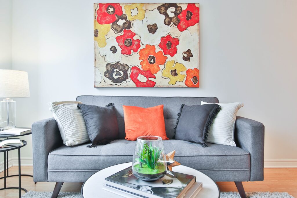  orange, grey and white throw pillows on a cushioned sofa by the wall